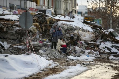 People sit by a collapsed building in Malatya, Turkey (AP photo)