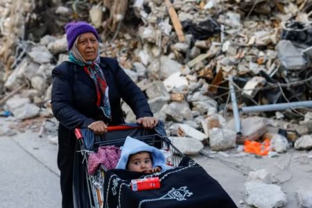 A woman pushes a shopping cart with a child, in the aftermath of a deadly earthquake, in Hatay, Türkiye Feb 11, 2023. (Photo: REUTERS/Kemal Aslan)