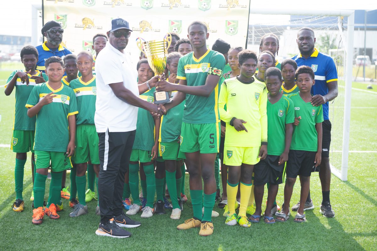 GFF Technical Director Bryan Joseph handing over the championship trophy to the East Coast Demerara captain in the presence of teammates and the coaching staff after winning Tiger Rentals U13 Football title