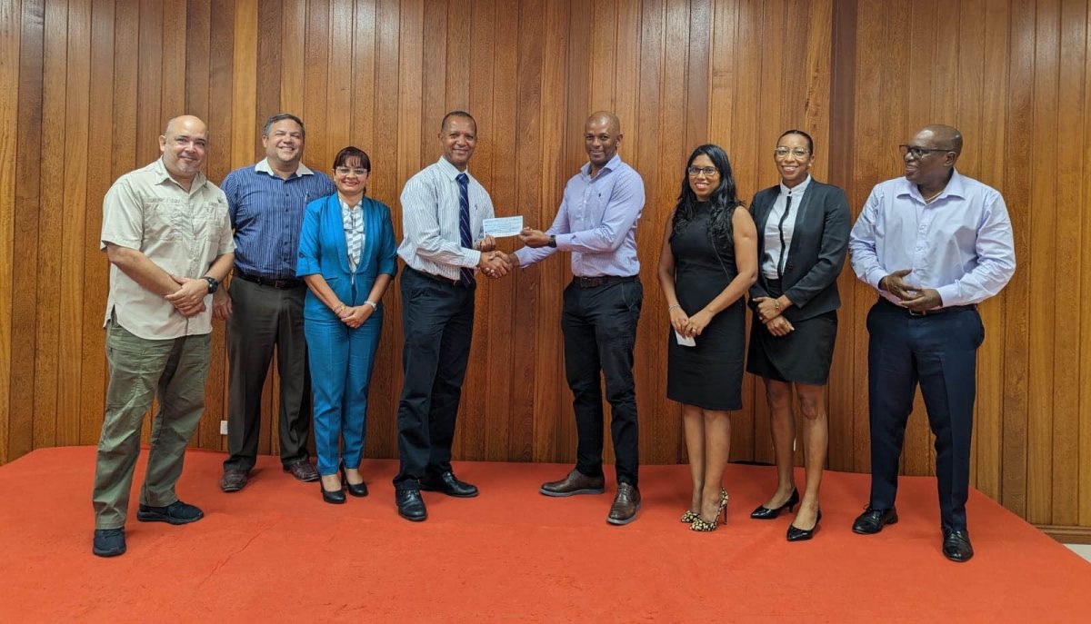 President Godfrey Munroe in centre hands over sponsorship cheque to Aubrey Hutson, flanked by Executive Members of the Guyana Olympic Association. From left to right: Michael Singh, Philip Fernandes, Emily Ramdhani, Aubrey Hutson, Godfrey Munroe, Vidushi Persaud-McKinnon, Cristy Campbell and Steve Ninvalle.
