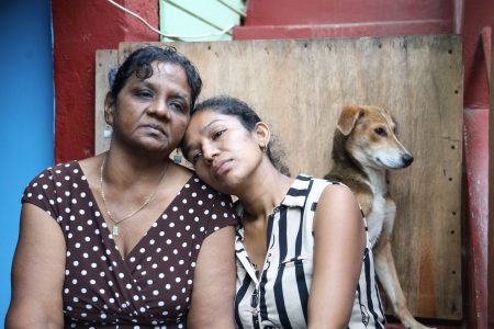 A grieving Linda Bajnath, left, comforts her daughter- in-law Parbatee Kumar at their Penal home yesterday, one day after her son Anand Kumar, grandson Kishore and son-in-law Rolly Hosein were killed.
