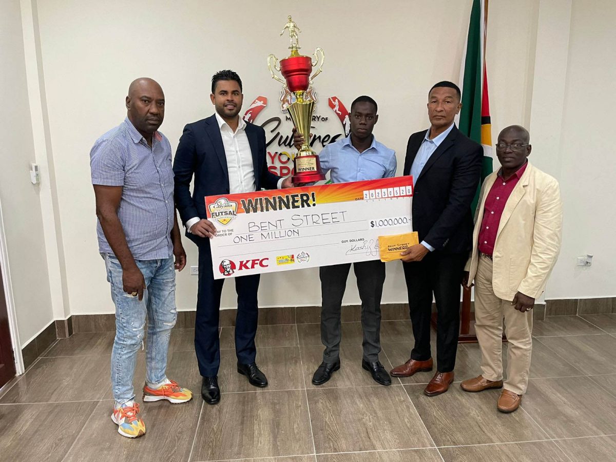 Bent Street Captain, Adrian Aaron receives his team’s One Guyana Futsal first prize  from Minister Charles Ramson Jr., watched by from left, Frank `English’ Parris, Kashif Muhammad, Chairman of the National Sports Commission and former national hockey player Colin `BL’ Aaron.