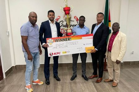 Bent Street Captain, Adrian Aaron receives his team’s One Guyana Futsal first prize  from Minister Charles Ramson Jr., watched by from left, Frank `English’ Parris, Kashif Muhammad, Chairman of the National Sports Commission and former national hockey player Colin `BL’ Aaron.