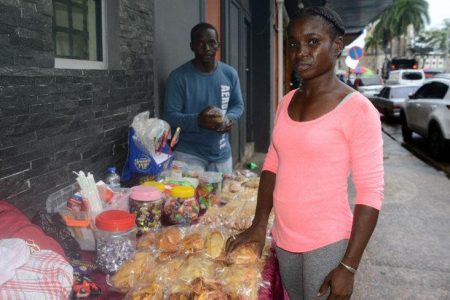 Guyanese nationals Candy Oudkerk and her husband, Paul Benjamin, arrange homemade treats for sale on Independence Square, Port of Spain, yesterday. The couple empathised with the parents of 19 children who perished in the dorm fire in Guyana. —Photo: Ishmael Salandy