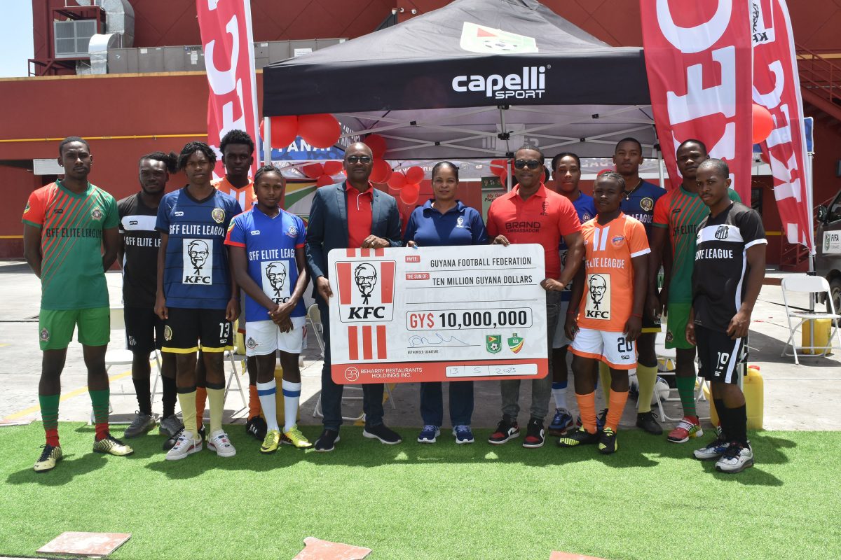 GFF President Wayne Forde receives the sponsorship cheque from KFC’s Marketing Manager Pamela Manasseh in the presence of representatives from the respective teams