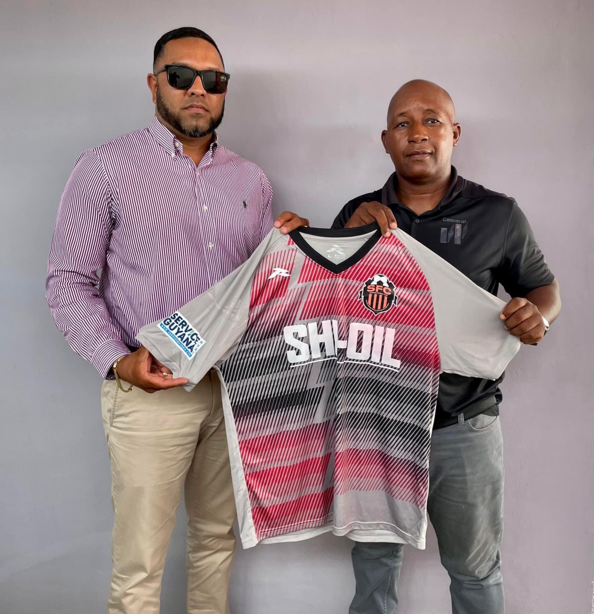 Javed Ali (left), President of Slingerz FC displaying the new team jersey alongside GFA President Otis James.
