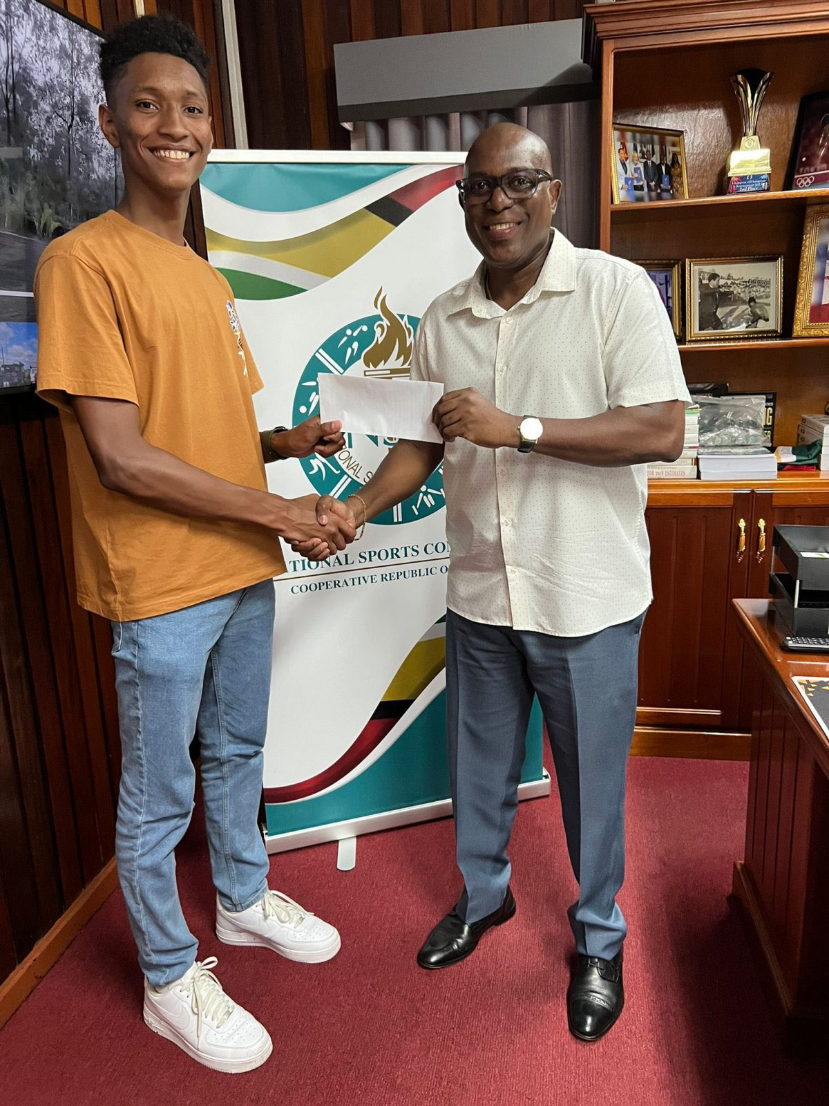 Five time CARIFTA Games gold medalist Raekwon Noel (left) receiving financial support from the Ministry of Culture, Youth, and Sport and the National Sports Commission from Director of Sports Steve Ninvalle