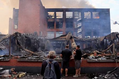 People look at a building of the Tessi group, burnt during night clashes between protesters and police, following the death of Nahel, a 17-year-old teenager killed by a French police officer in Nanterre during a traffic stop, at the Alma district in Roubaix, northern France, June 30, 2023