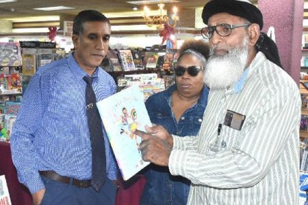 Umar Abdullah ,right founder leader of The First Wave Movement displays a children’s book titled I Am a Rainbow while speaking to reporters on Thursday about the content of the book on sale at RIK Services Ltd. bookstore on High Street, San Fernando . Looking on is Ruby Jemm and an offical of the bookstore. Abudullah is objecting to the sale of book at the bookstore. Photo:TREVOR WATSON