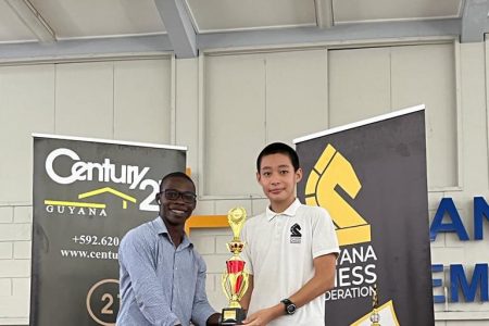 Queen’s College student Alexander Zhang receives the Century 21 trophy for winning the 2023 Under-16 Chess Championship of Guyana