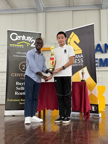 Century 21 representative Tyrell John (left) presenting the Open Divisional championship trophy to winner Alexander Zhang 