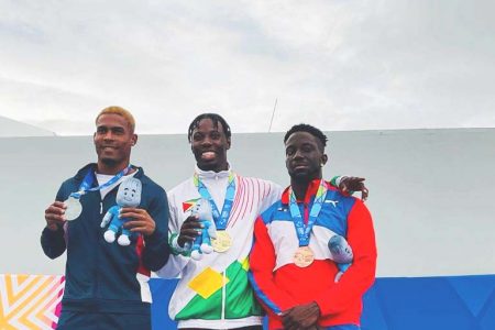 Emanuel Archibald (centre) is all smiles as he stood atop the podium after receiving his gold medal for winning the men’s 100m on Monday evening alongside silver medalist Jose Gonzalez (left) of the Dominican Republic and bronze winner Rikkoi Brathwaite of the British Virgin Islands 