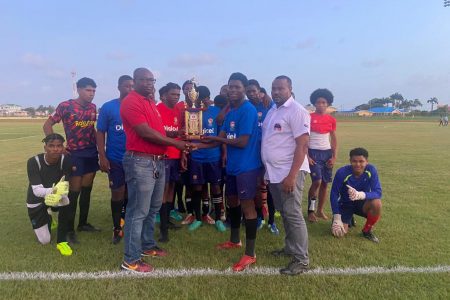 Region #3 coordinator Adrian Giddings (left) presenting the championship trophy to the captain of Westminster in the presence of teammates after defeating Leonora to win the zonal title