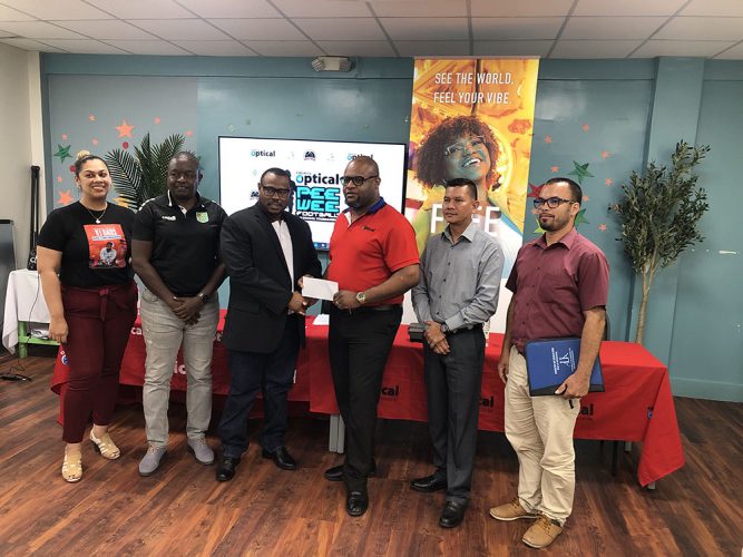 Troy Mendonca (3rd from left), Co-Director of the Petra Organization, receiving the sponsorship cheque Richard Simpson, Courts Optical Chain Manager, in the presence of Christel Van Sluytman (1st from left), Senior Brand Manager of Courts Guyana, GFF Technical Director Brian Joseph (2nd from left), Marti DeSouza (2nd from right), Deputy Chief Education Officer (Hinterland), and Nicholas Fraser, Head of Allied Arts of the Ministry of Education 
