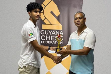Queen’s College student Kyle Couchman (left ) receives his first place trophy from an employee of Jade’s Wok which sponsored the Guyana Chess Federation’s Developmental Chess Tournament. In the five-round tournament, Couchman scored a total of 4.5 points. He drew with National Junior champ Keron Sandiford.  