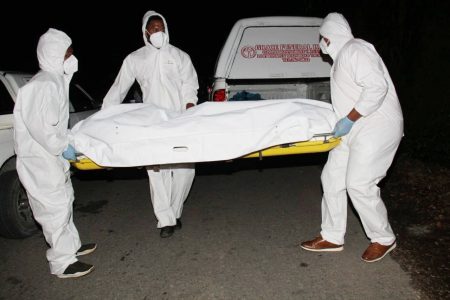 Undertakers remove one of the murder victims from Lalaja Junction, Blanchisseuse Road, Arima, last night.