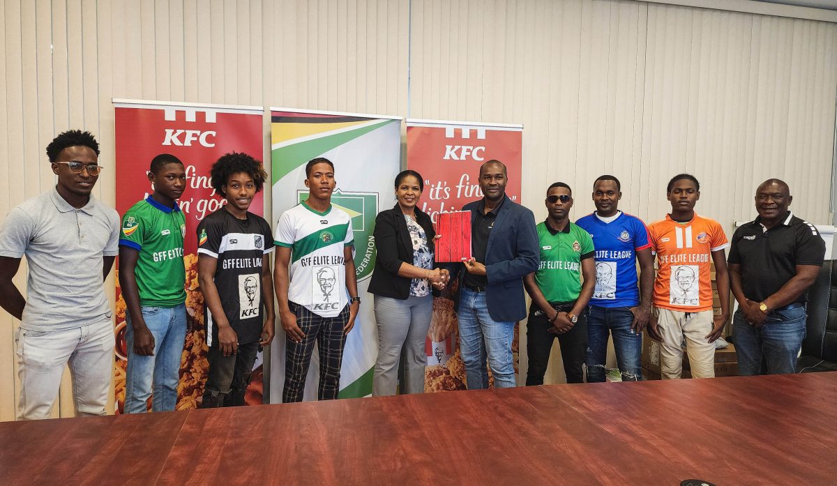 KFC Guyana Marketing Manager Pamella Manasseh (center) presents the sponsorship package to GFF President Wayne Forde in the presence of representatives from several of the competing teams.