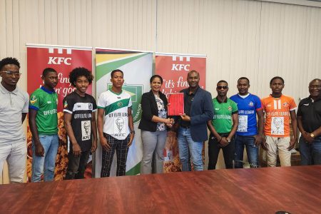 KFC Guyana Marketing Manager Pamella Manasseh (center) presents the sponsorship package to GFF President Wayne Forde in the presence of representatives from several of the competing teams.