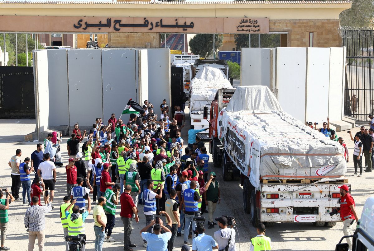 Egyptian volunteers gather and celebrate with a Palestinian flag next to trucks carrying humanitarian aid from Egyptian NGOs driving through the Rafah crossing from the Egyptian side, amid the ongoing conflict between Israel and the Palestinian Islamist group Hamas, in Rafah, Egypt October 21, 2023. REUTERS/Stringer