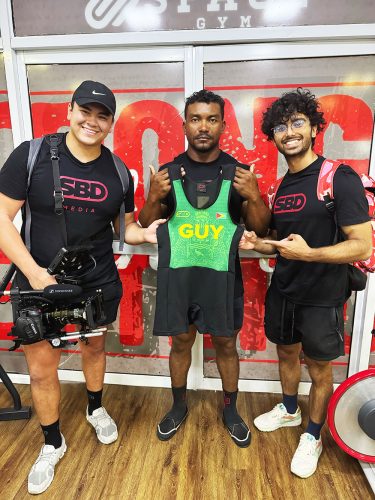 Carlos Peterson-Grifith (centre) becomes the first Guyanese to be outfitted with
official SBD apparel customised with the nation’s colours. He is flanked by SBD’s Justin Nutt (left) and Zalim Farooqui, who arrived in Guyana recently from the
USA to film the power-lifter as part of the ‘Road to Sheffield’ documentary.