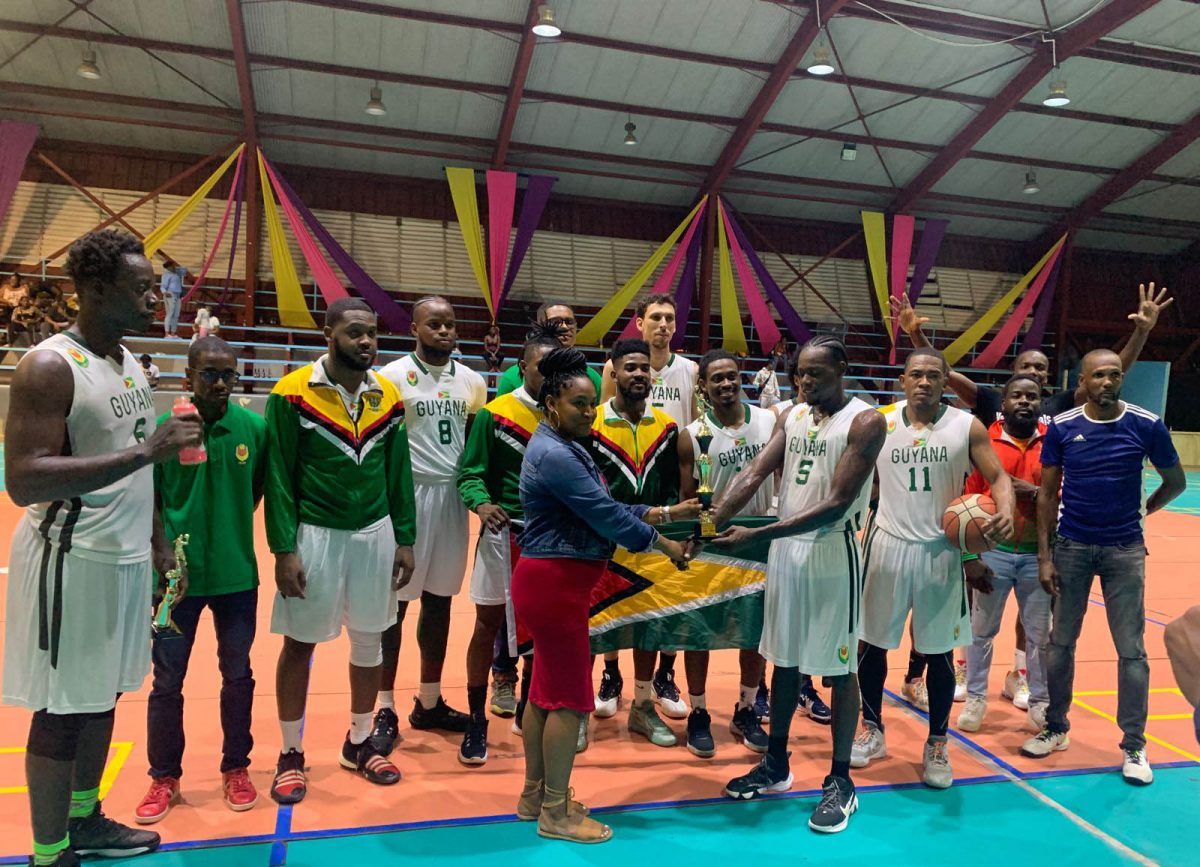 Dianna Khan, wife of late basketball stalwart and GDF Warrant Officer Jason Khan, presents the trophy, which was named after her husband, to Guyana’s captain Harold Adams in the presence of teammates and coaches following their victory over Suriname