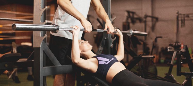 A woman bench pressing with a spotter (Image by Freepik)