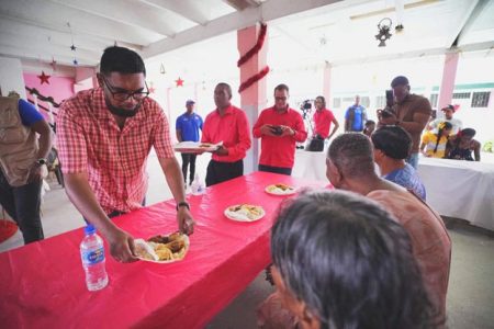 President Irfaan Ali recently served lunch to senior citizens at the Dharm Shala home for the benevolent in Albouystown and distributed toys to children in the community. The President is seen serving one of the senior citizens. (Photo taken from the president’s Facebook page)
