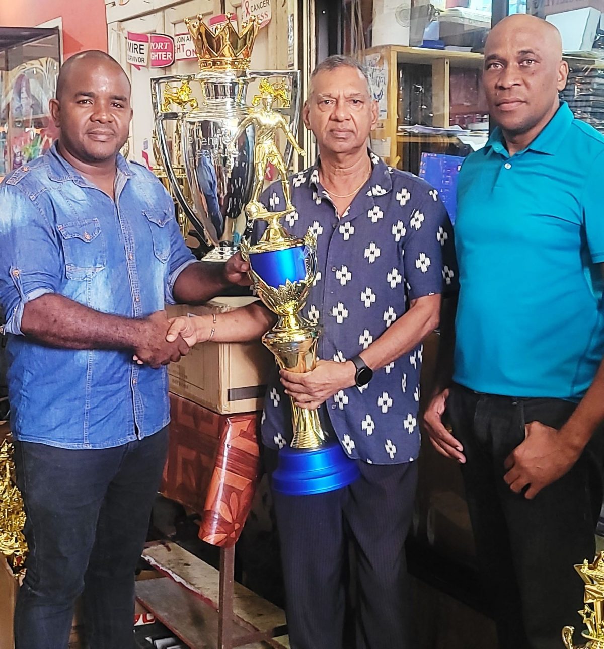 Trophy Stall proprietor Ramesh Sunich (centre) presents the championship trophy to tournament consultant Keeran Williams in the
presence of referees coordinator Stanley Lancaster
