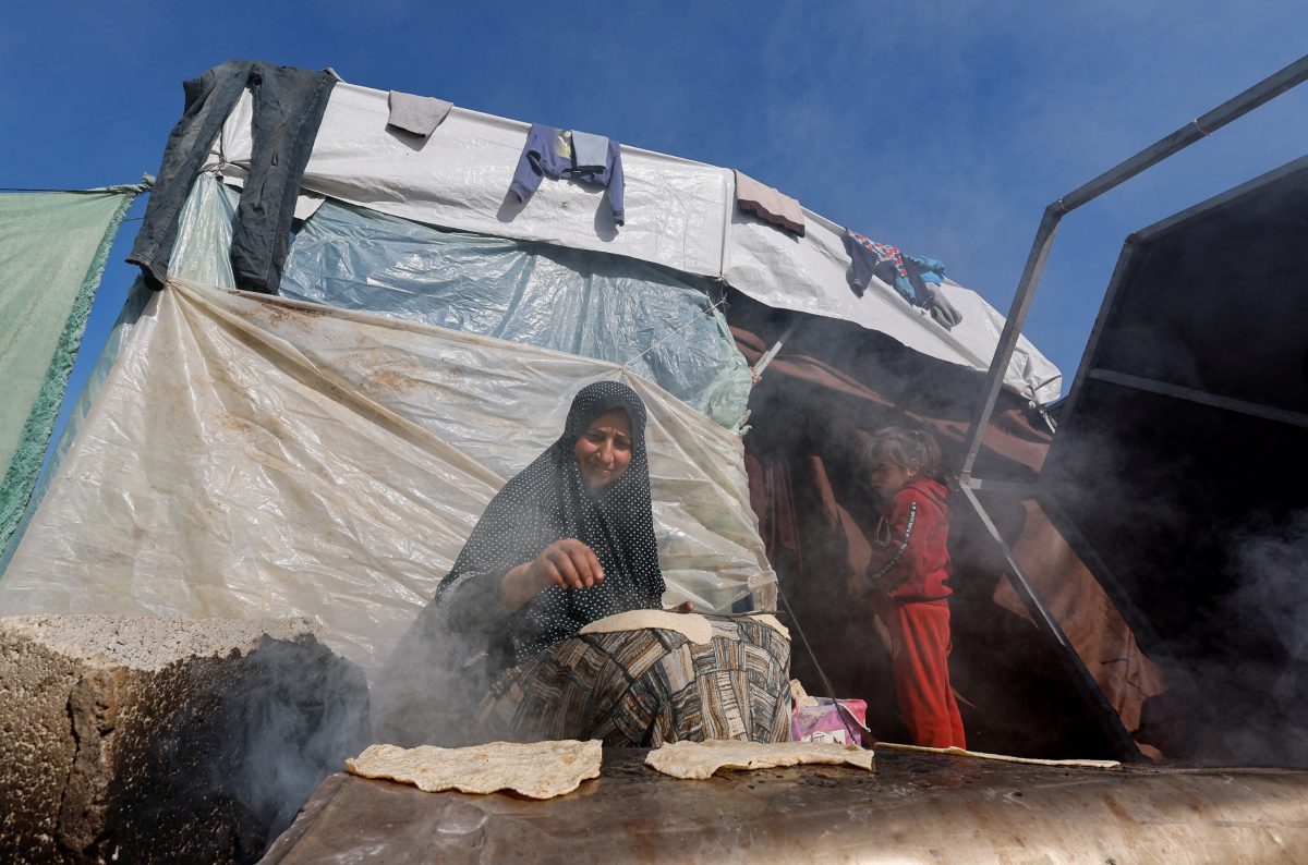 A child stands next to a cooking woman, as displaced Palestinians, who fled their houses due to Israeli strikes, shelter in a tent camp near the border with Egypt, amid the ongoing conflict between Israel and the Palestinian Islamist group Hamas, in Rafah in the southern Gaza Strip, December 11, 2023. REUTERS/Mohammed Salem