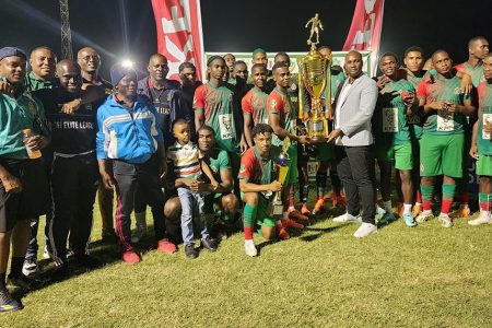 GDF captain Kenard Simon receives the
championship trophy from GFF President Wayne Forde in the presence of teammates and coaches after defeating the Western Tigers via penalty kicks