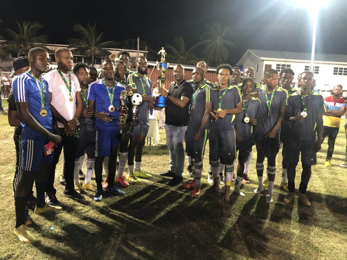 GFF President Wayne Forde presents the championship trophy to the captain of Monedderlust FC in the presence of teammates following the team’s victory over Slingerz FC in the Elite League Playoff final.