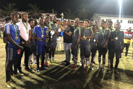 GFF President Wayne Forde presents the championship trophy to the captain of Monedderlust FC in the presence of teammates following the team’s victory over Slingerz FC in the Elite League Playoff final.