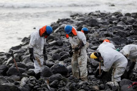 Workers clean up an oil spill at the beach as demonstrators take part in a protest outside Repsol’s La Pampilla refinery against the recent oil spill that has caused an ecological disaster on the coasts of Lima, in Ventanilla, Peru January 29, 2022. REUTERS/Angela Ponce/File Photo