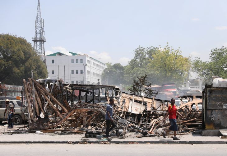 People walk past remains of vehicles near the presidential palace, after they were set on fire by gangs, as violence spreads and armed gangs expand their control over the capital, in Port-au-Prince, Haiti March 25, 2024. REUTERS/Ralph Tedy Erol/ File Photo