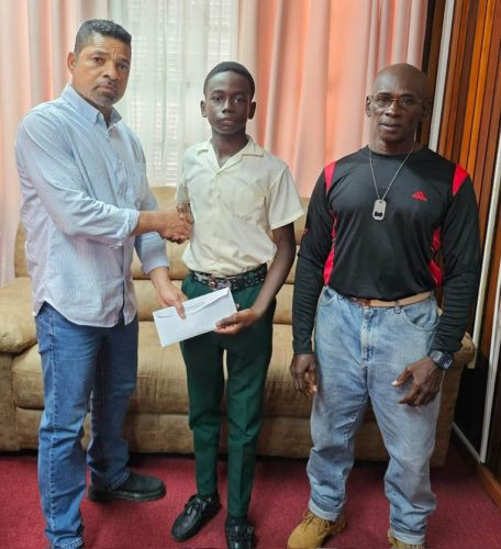 U-16 standout Keyon Britton (centre) receives the donation from USA-based Guyanese Samuel Gittens (left) in the
presence of his coach, Clifton Moore
