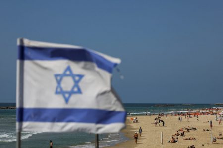 An Israeli flag flutters as people rest on the beach, after Iran launched drones and missiles towards Israel, in Tel Aviv, Israel, April 14, 2024. REUTERS/Hannah McKay