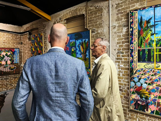 Dennis de Caires (right) in conversation, paintings from his exhibition Wuh
Part You Is? in the background (Photo: Barbados Museum & Historical Society)