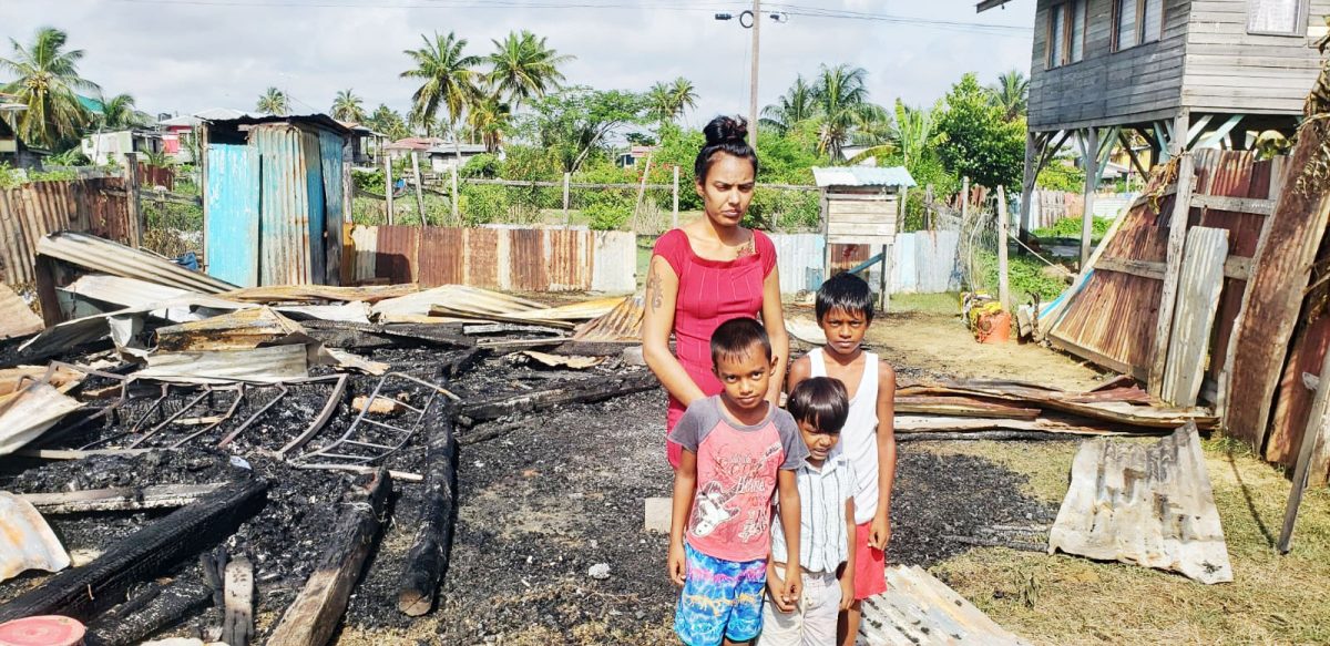 Hemwattie Brijbhukan and her children in front of the burnt ruins of their home
