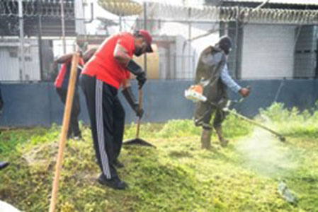 The president raking the grass as it is cut by community enhancement workers