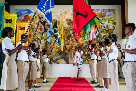 The Queen’s College school yesterday officially recognised it’s 180 year rich history with a ceremony at the National Cultural Centre addressed by President Irfaan Ali and others. Here, current students with the various athletic house flags form an arch over the red carpet. (Ministry of Education photo)