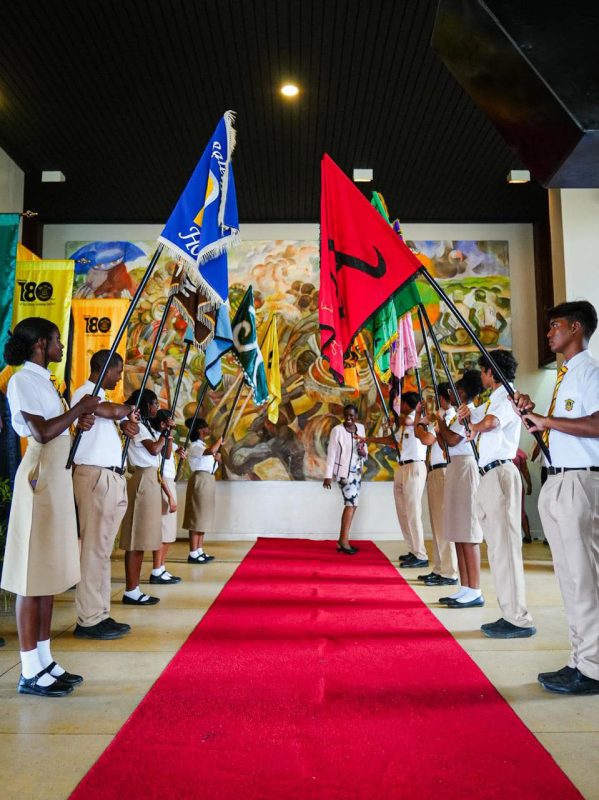 The Queen’s College school yesterday officially recognised it’s 180 year rich history with a ceremony at the National Cultural Centre addressed by President Irfaan Ali and others. Here, current students with the various athletic house flags form an arch over the red carpet. (Ministry of Education photo)