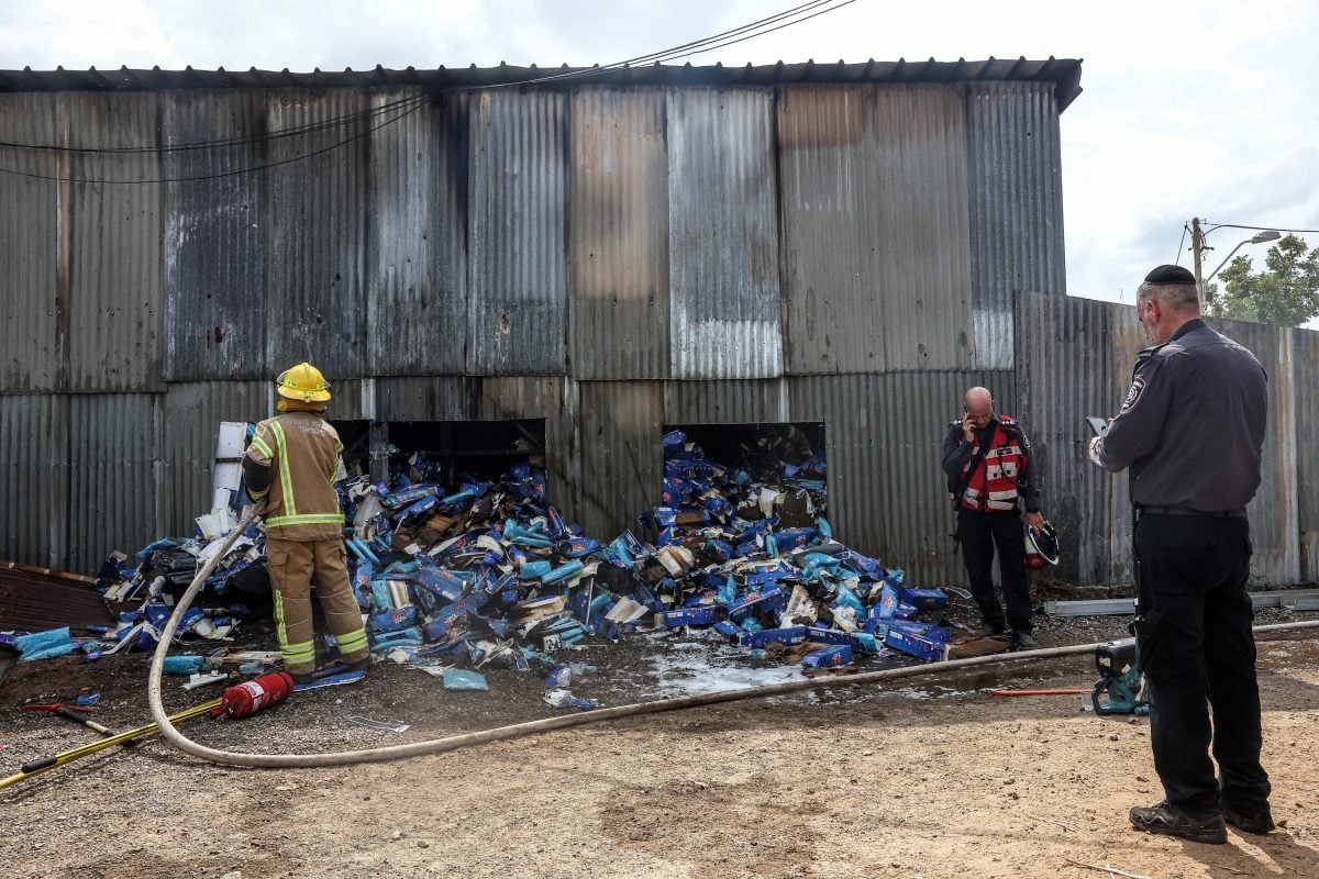 An Israeli police officer looks on as an Israeli firefighter works at the scene where a projectile landed, after Hamas’ armed wing said it attacked Tel Aviv with a missile salvo, amid the ongoing Israel-Hamas conflict, in Kfar Chabad, Israel, October 7, 2024. REUTERS/Itai Ron