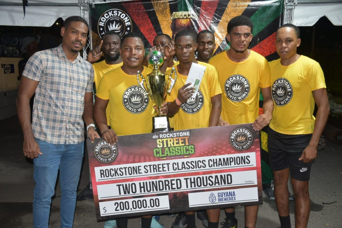 Ballerz Empire displaying their spoils alongside Guyana Brewery’s marketing manager, Seweon McGarrell, after defeating Jetty Gunners to win the maiden edition of the Rockstone Street Classic